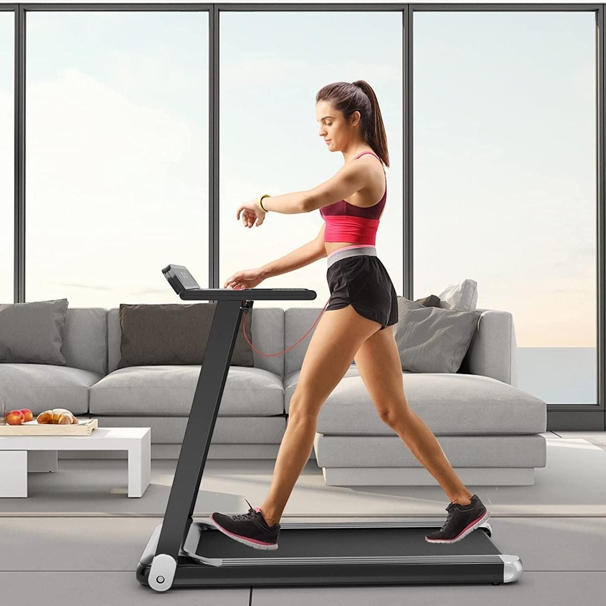 Femme marchant sur un tapis de course électrique pliable Alvore dans un salon moderne et lumineux.